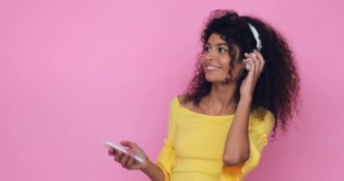 Kulaklıklı mutlu bir kadın dans ediyor ve elinde pembe bir telefon tutuyor.