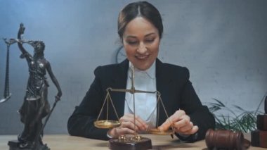 Gülümseyen avukat terazi kullanıyor ve ofisteki kameraya bakıyor. 
