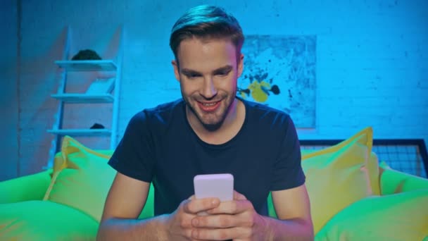 Homme Souriant Utilisant Smartphone Sur Canapé Pendant Soirée — Video