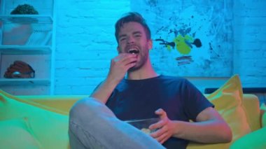 Neşeli adam patlamış mısır yiyor ve televizyon seyrediyor. 