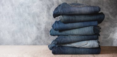 Gri arka planda katlanmış kot pantolon yığını. Boşluğu kopyala