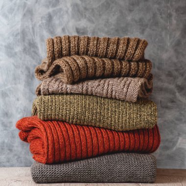 Gri arka planda katlanmış yün kadın kazakları ve eşarpları. Sıcak giysi mevsimi. Moda konsepti