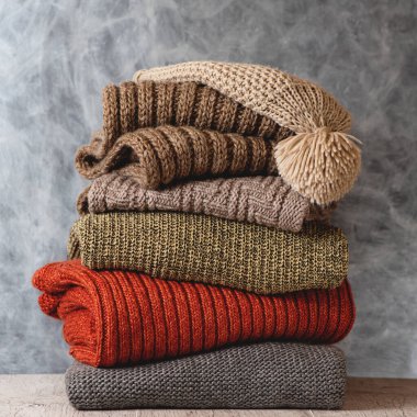 Katlanmış yün kadın süveter, atkı ve gri arka planda ponpon şapkası yığını. Sıcak örgü giyme mevsimi. Moda konsepti