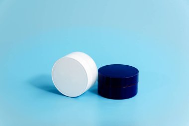 Açık mavi arka planda iki kapalı plastik krema kavanozu. Boş beyaz ve mavi kozmetik kaplar. Gece gündüz yüz bakımı konsepti. Güzellik ürünlerinin markası. Modelleme. Boşluğu kopyala