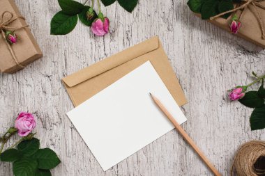 Gri masaya kraft kağıdı ve pembe gül çiçekleriyle sarılı bir hediye kutusu. Metin için boş bir kağıt. Üst Manzara. Düz yatıyordu. Boşluğu kopyala
