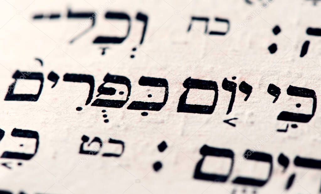 Closeup of hebrew words Yom Kippur in Torah page that translate in english as Day of Atonement, holiest day of the year in Judaism. Selective focus