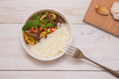 Biberli biftek ve beyaz pirinç. Beyaz tabak, arka planda sarımsak. Menüdeki Lezzetli bir yemeğin üst görüntüsü.