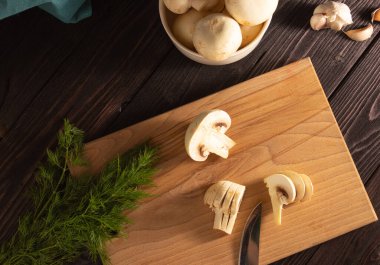 Tahta kesme tahtasının üzerinde doğranmış mantar. Dill, mantarlar arka planda. Vejetaryen yemeği pişirmek. Yukarıdan görünüşü.