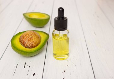 Cam bardakta avokado yağı ve beyaz ahşap arka planda avokado meyvesi. Sağlıklı gıda, deri ve vücut bakımı, vejetaryenlik.