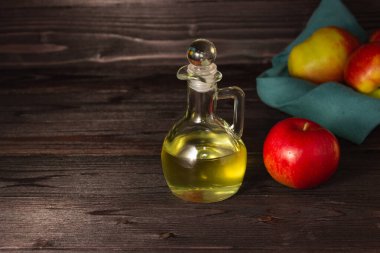 Elma şarabı sirkesi. Koyu ahşap bir masada cam bir sürahide. Elmalar yakında. Boş alan.
