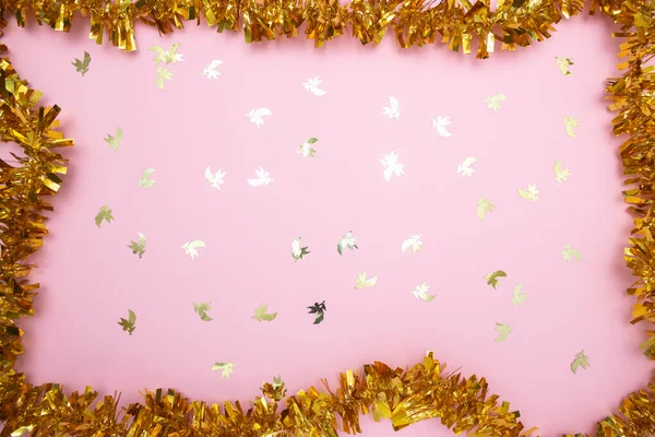 A scattering of Golden angel figures and a garland on a pink background. Christmas, holidays, New Year.