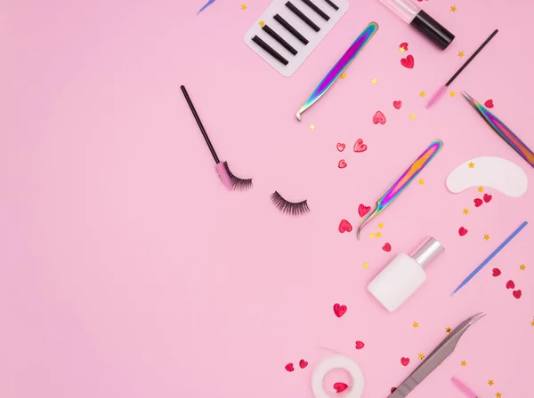 Eyelash extension tools, artificial eyelashes and red hearts on a pink background. Tools for the lashmaker. Top view, copyspace.