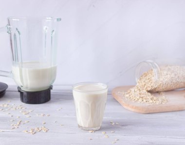Hafif arka planda cam bir fincanda sebze yulaf sütü. Blender kasesi arka planda. Bitkisel sütün hazırlanması. Sağlıklı içecekler, vejetaryenlik. Yan görünüm.