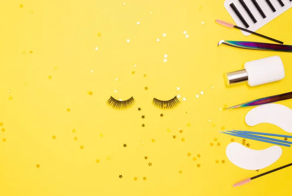 Eyelash extension tools and artificial eyelashes on a yellow background. The view from the top.