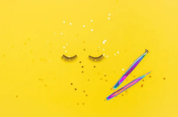 Tweezers for eyelash extension and artificial eyelashes on a yellow background. Tools for the lashmaker. The view from the top.