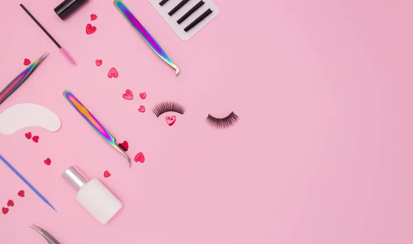 Eyelash extension tools, artificial eyelashes and red hearts on a pink background. Tools for the lashmaker. Top view, copyspace.