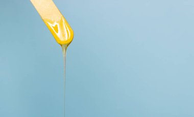 Tahta bir spatuladan şeker tüy dökücü macun damlıyor. Vücut kıllarının alınması. Metin için boş alan, mavi arkaplan.