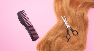 Pembe arka planda kırmızı yapay saç, tarak ve makas. Saç stili, saç kesimi, saç bakımı..