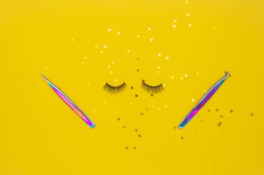 Kirpik uzatma için cımbız ve sarı arka planda yapay kirpikler. Kirpikçi için aletler. Yukarıdan görünüşü.