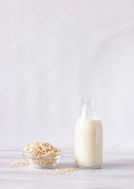 Cam şişede sebze yulaf sütü ve arka planda yulaf ezmesi. Sağlıklı içecekler, vejetaryenlik. Yan görüş. Dikey fotoğraf