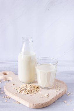 Cam şişedeki sebze yulaf sütü ve tahta kesme tahtasındaki cam bardakta. Sağlıklı içecekler, vejetaryenlik. Yan görüş. Dikey fotoğraf