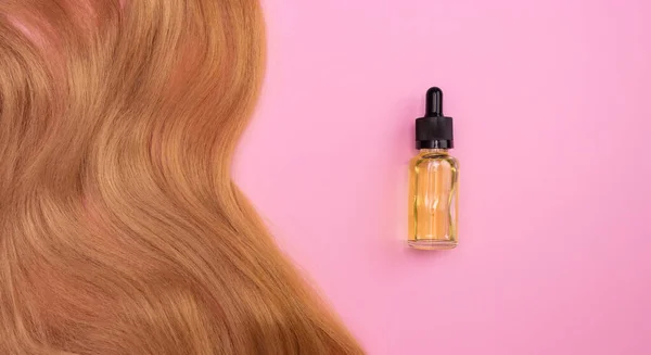 Brown artificial hair on a pink background and cosmetic oil in a glass bottle with an eyedropper. The concept of a hair salon, haircut, hair care.