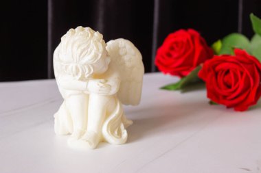 Siyah arka planda kırmızı bir gül ve kanatlı küçük bir melek heykeli. Cenaze, taziye ve yas kavramı..