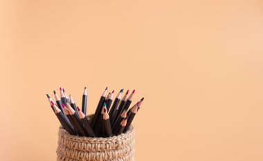 Bej arka planda jütten yapılmış hasır sepetteki renkli kalemler. Yürütme Ofisi