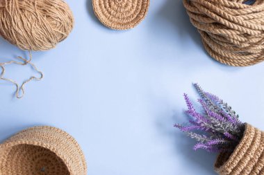The knitted part of the basket made of jute rope and the crochet hook on a blue background, free space. Hobbies, needlework, organization of space.