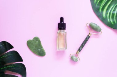 Jade gua sha kazıyıcı, patenli yüz masajı ve canavar yapraklı kozmetik yağ. Kişisel bakım kavramı. Yüz bakımı. Sıfır kayıp. Evde kaldırma ve tonlama tedavisi.