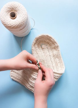 Eller mavi arka planda beyaz pamuktan yapılmış bir çanta örer. Hobi, el yapımı..