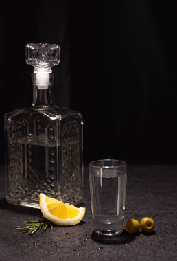 Bir sürahi ve küçük bir bardak votka ya da siyah arka planda diğer renksiz alkollü içecekler. Bir dilim limon..