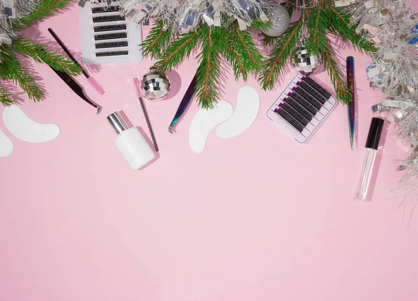 New year and Christmas for the masters of eyelash extension. Things for the work of lashmakers, artificial eyelashes, tweezers, combs, brushes for extended eyelashes. Top view, pink background, free space for text.