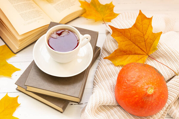 Autumn atmosphere. A cup of tea, yellow maple leaves, books, and a knitted thing