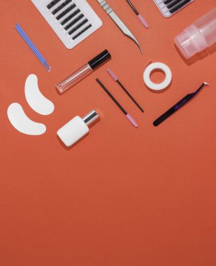 Turuncu arkaplanda kirpik uzatma araçları, metin için boş alan, üst görünüm. Yapay kirpikler, cımbızlar, mikro fırçalar, lashmaker için yamalar ve fırçalar..