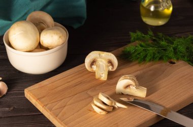 Tahta kesme tahtasının üzerinde doğranmış mantar. Dill, mantarlar arka planda. Vejetaryen yemeği pişirmek.