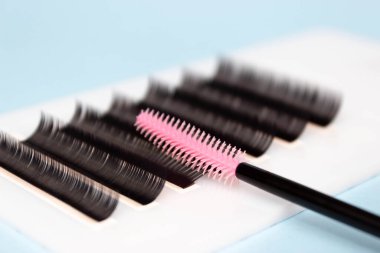 Kirpik eklentileri, lashmaker aletleri. Beyaz tablet üzerindeki yapay kirpikleri ve pembe silikon fırça tarağını kapat..