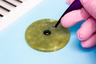 Cımbızla bir el ve bir demet yapay kirpikler onları yapıştırıcıya düşürür. Lashmaker 'ın işi, kirpik eklentileri.