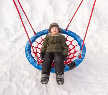 Bir çocuk kışın salıncakta sallanır. Çocuklarla kış yürüyüşleri, eğlence.