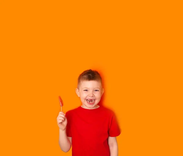 Niño Come Una Piruleta Forma Corazón Sobre Fondo Naranja Diversión —  Fotos de Stock