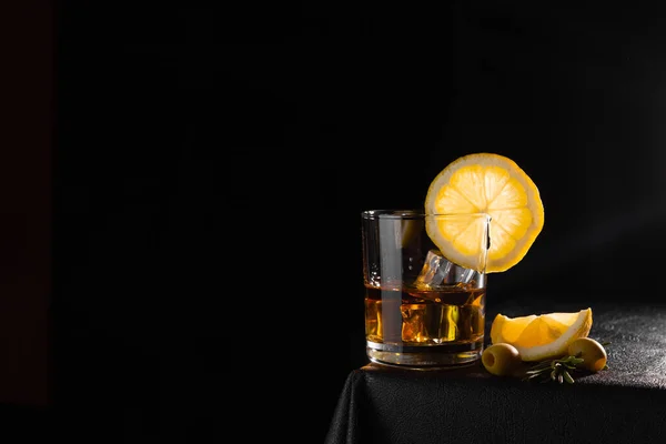 テーブルの上の黒い背景にガラスのコニャック オリーブとレモンのスライス アルコールだ コピースペース サイドビュー — ストック写真