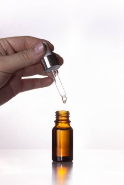 Cam kavanoz ve beyaz arka planda pipeti olan el. Kozmetik, cilt bakımı.