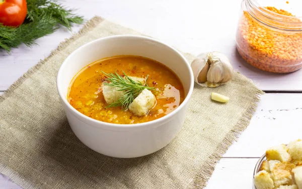 Red lentil soup with ingredients on a light background. Traditional Turkish or Arabic spicy lentil and vegetable soup, healthy vegan food. Side view