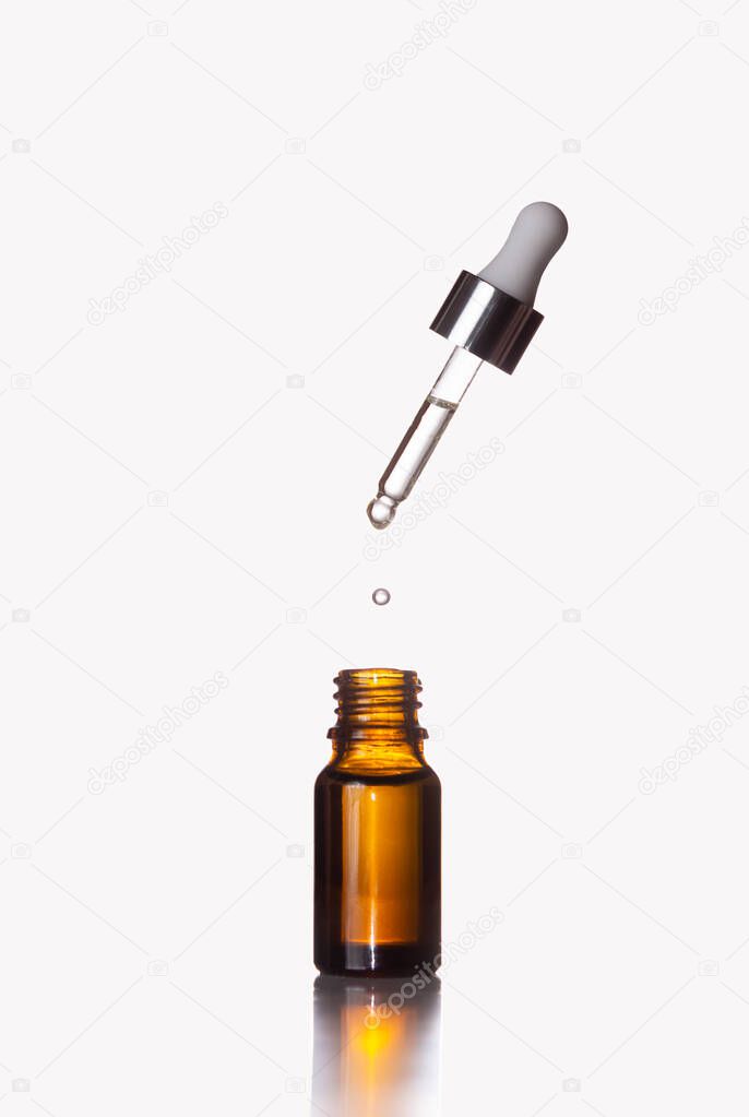 A glass jar and a flying dropper with a drop on a white background. Cosmetics, skin care.