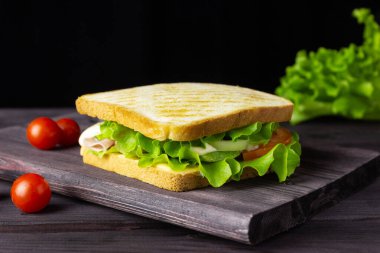 Sandwich with white bread, lettuce and vegetables on a dark background. A quick healthy snack.