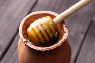 Bee honey in a clay pot on a wooden table. Wooden spatula for honey. Side view, close up. Healthy food. Farm, apiary.