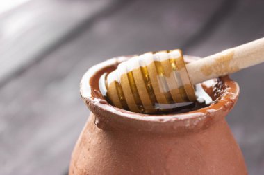 Bee honey in a clay pot on a wooden table. Wooden spatula for honey. Side view, close up. Healthy food. Farm, apiary.