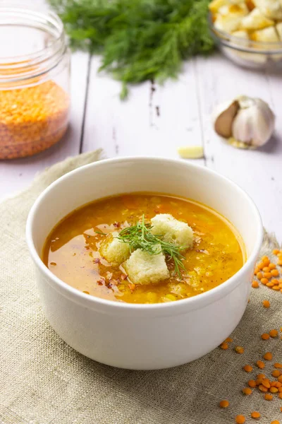 Red lentil soup with ingredients on a light background. Traditional Turkish or Arabic spicy lentil and vegetable soup, healthy vegan food. Side view, vertical orientation.