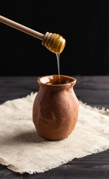 Bee honey flows down from a wooden spoon into a homemade clay pot. Farming, apiary, healthy food.