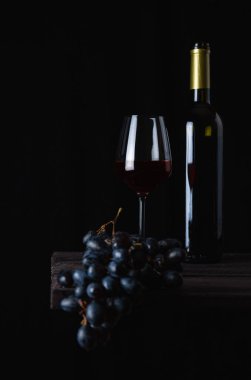 Bir şişe kırmızı şarap, arka planda bir bardak ve üzüm..